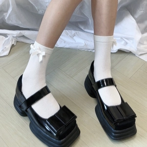 Dettaglio di calze a rete bianche con fiocchi abbinate a scarpe Mary Jane nere lucide