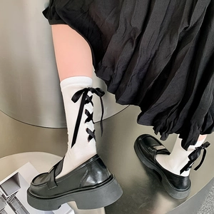 Détail de chaussettes mi-mollet blanches avec rubans lacés noirs et mocassins à plateforme