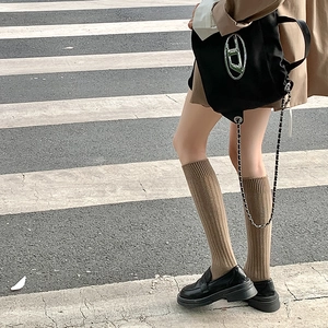 Primer plano de calcetines de punto acanalado marrón con mocasines de cuero negro y bolso metal