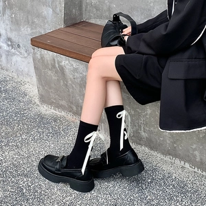 Détail de chaussettes hautes noires style Lolita avec nœuds en soie et chaussures à plateforme