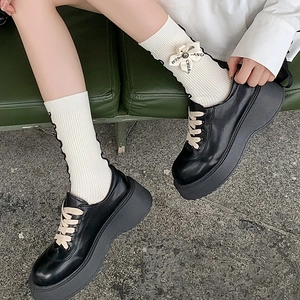 Detail of black platform leather loafers with white bow socks and metallic buckle