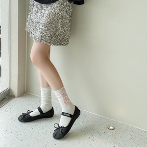 Détail de chaussettes blanches à trois nœuds roses portées avec des ballerines noires