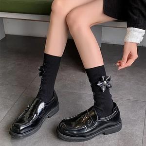 Detail of black ribbon bow with letter print on knitted crew socks and patent loafers