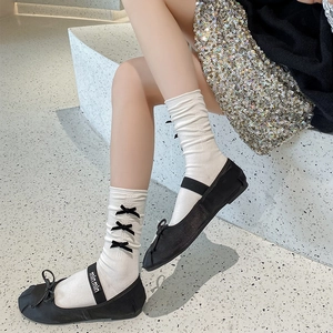 Détail de chaussettes mi-mollet blanches à nœuds noirs et chaussures Mary Jane en satin
