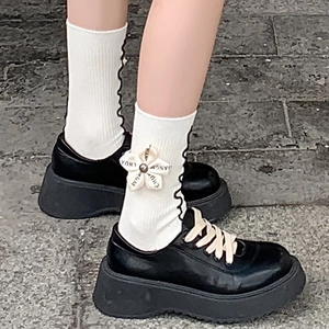 Detailed shot of white ribbed socks with floral charm and black platform loafers