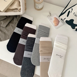 Close-up of rib-knit cotton slouch socks in six neutral colors with branded packaging