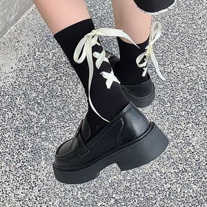 Détail de chaussettes mi-mollet Lolita noires avec nœuds en ruban crème et chaussures compensées