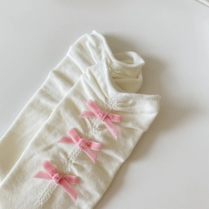 Gros plan de chaussettes en tricot blanc avec trois nœuds en velours rose sur le côté