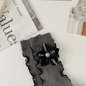 Close-up of grey knitted socks featuring scalloped edges and black ribbon flower details