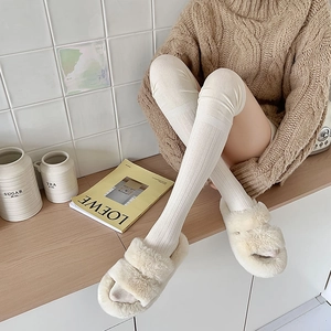 Close-up of white ribbed knit over-the-knee socks paired with fuzzy plush slippers