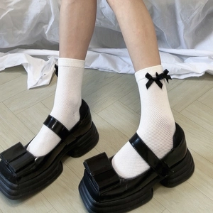 Dettaglio di calze a rete bianche con piccoli fiocchi neri e scarpe con plateau alto