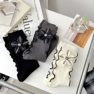 Macro view of knit leg warmers with floral ornaments and wavy ruffle trim in neutral tones