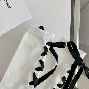 Détail de bas en maille côtelée blanche avec laçage en ruban noir et nœud