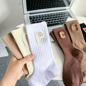 Detail of ribbed mid-calf cotton socks with varsity letter C embroidery in earth tones