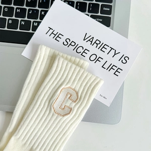 Detail of cream rib-knit mid-calf cotton socks featuring an embroidered C letter