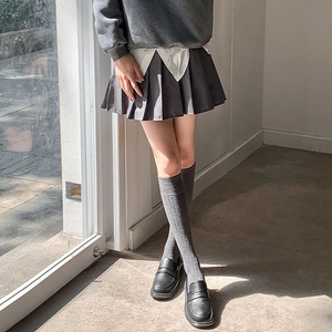 Détail de chaussettes hautes blanches à rayures portées avec une jupe plissée grise