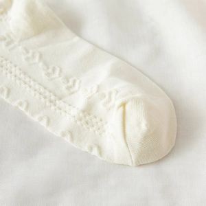 Vista macro di calzini in maglia di cotone bianco crema con delicati ritagli a cuore