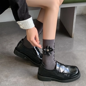 Detail of grey knit socks with black 3D flower trim paired with glossy loafers