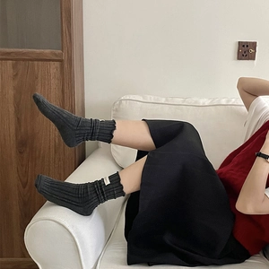 Detail of dark grey ribbed socks with frill cuffs and small tag on a white sofa