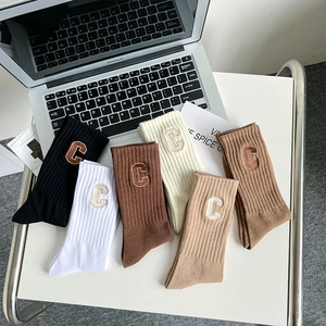 Flat lay of six cotton blend crew socks in neutral tones with embroidered C letter detail