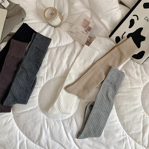 Détail de six paires de chaussettes hautes en tricot côtelé aux tons neutres sur un lit