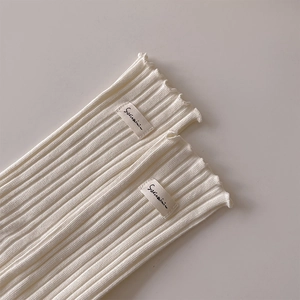 Detail of ribbed knit cream socks featuring a wavy lettuce edge and minimalist fabric label