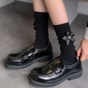 Black ribbed crew socks with bow accents paired with glossy patent leather loafers