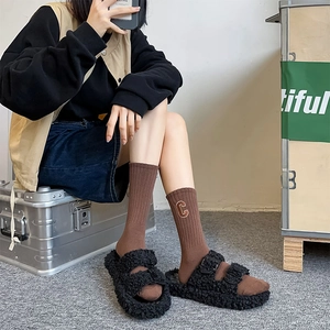 Close-up of brown ribbed knit mid-calf socks with embroidered letter C and black plush sandals
