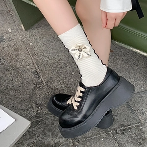 Detail of white ribbed socks with bow accent and black platform loafers in outdoor setting