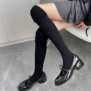 Detail of black knit over-the-knee socks with ribbed texture and glossy Mary Jane shoes