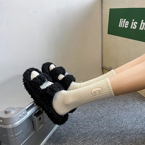 Close-up of black fuzzy faux fur double-buckle sandals worn with white mid-calf socks