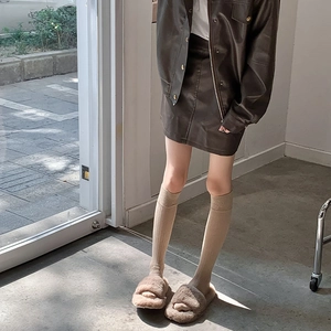 Détail de chaussettes montantes blanches à rayures avec jupe en cuir et pantoufles