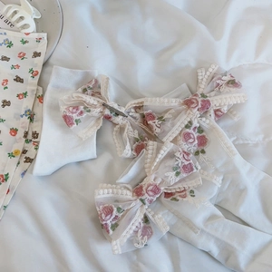 Dettaglio di calze bianche con fiocco in pizzo, ricami di rose rosa e accenti floreali