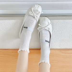 Close-up of white Mary Jane shoes with bows and sweet frilly floral socks on wooden floor