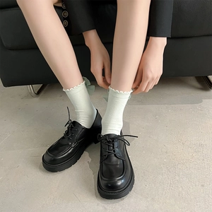 Détail de chaussettes blanches à volants avec nœuds verts et richelieus noirs à plateforme
