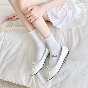 Detailed view of white Mary Jane ballet flats with lace butterfly socks on a cozy bed