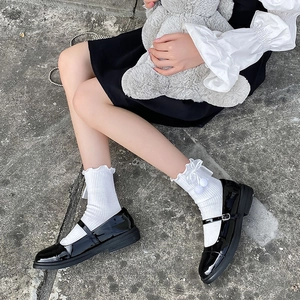 Détail de chaussettes blanches à volants et nœuds avec chaussures Mary Jane vernies noires