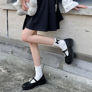 Détail de chaussettes Lolita blanches avec bords à volants, nœuds noirs et perles