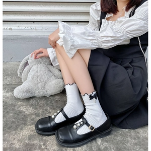 Détail de chaussettes blanches Lolita avec bords à volants, nœuds noirs et perles