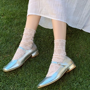 Silver metallic Mary Jane shoes with low heels and beige lace socks on green grass