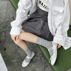 Détail de chaussettes grises côtelées avec ballerines blanches et jupe plissée