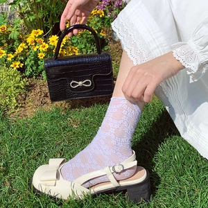 Detail of off-white Mary Jane sandals with lace socks and a black crocodile leather bag