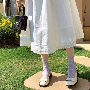 Close-up of lilac lace socks with white bow Mary Jane shoes in a garden setting