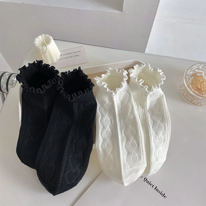 Detail of white and black ankle socks with ruffled edges and heart cable-knit pattern