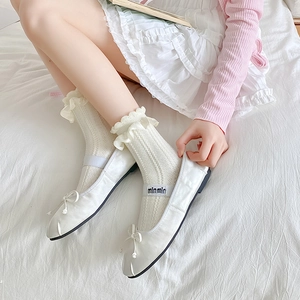 Gros plan de ballerines blanches avec rubans et chaussettes en dentelle sur drap blanc