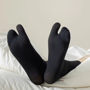 Detailed close-up of black split-toe socks with fine ribbed cotton texture on a bed