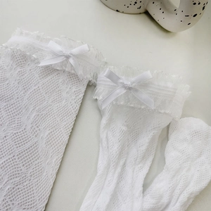 Detailed close-up of white lace mesh stockings with silk bows and double floral lace trim