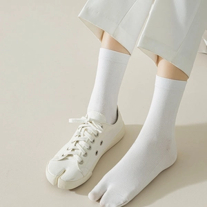 Close-up of white ribbed Tabi socks paired with matching split-toe canvas sneakers