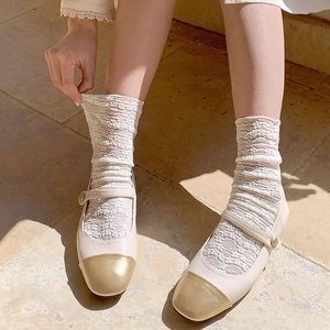 Beige Mary Jane shoes with gold toe caps and white lace floral socks on stone floor