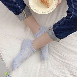 Detailed knit texture of light blue low-cut cotton socks with colorful flecks on bed